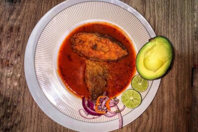 Plato con 3uGeOWMIbFM que muestra trozos de pescado en salsa roja acompañados de aguacate y rodajas de limón