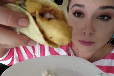 Primer plano de mujer sosteniendo un taco crujiente junto a un plato, 6sM7auILCXo