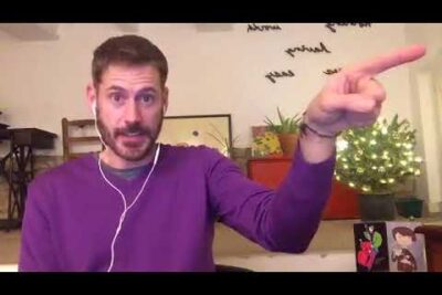 Hombre con suéter morado y auriculares señalando hacia la derecha en un ambiente hogareño 7Kvr1sIytFs.