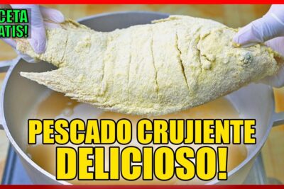 Pescado entero empanizado sostenido con guantes sobre una olla listo para freír 8Psay0Lhab4