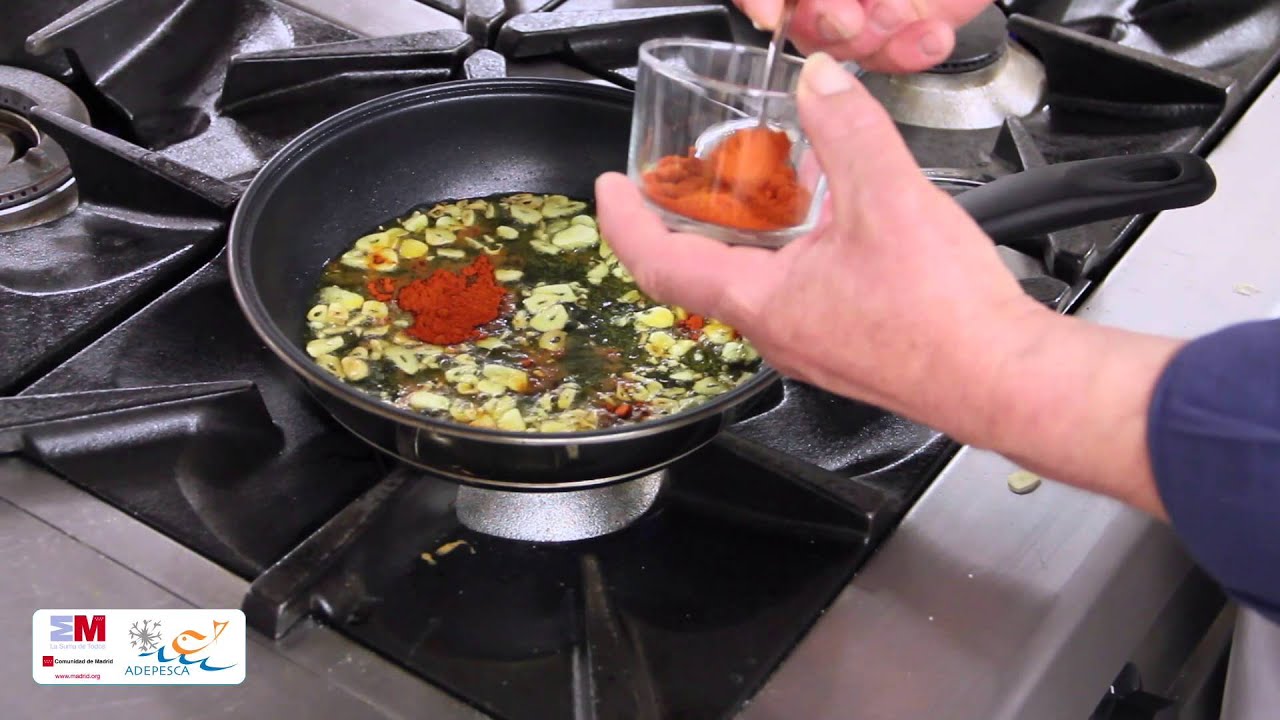 Mano añadiendo pimentón a una sartén con láminas de ajo en aceite hirviendo 97SvRSXehM0
