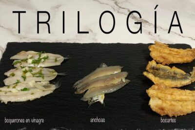 Presentación de tres preparaciones de pescado: boquerones en vinagre, anchoas y bocartes fritos sobre pizarra