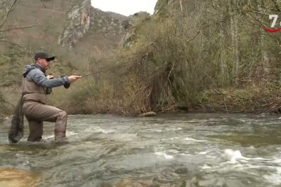 Pescador vadeando con waders y lanzando la caña en un río de montaña IqRCvUASMZE.