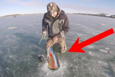 Pescador sobre hielo sacando una trucha arcoíris a través de un agujero con una flecha roja NQbnangRAyE