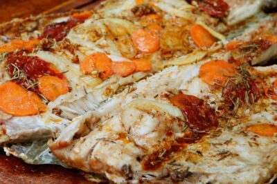 Pescado al horno con rodajas de zanahoria, cebolla y hierbas sobre tabla de madera