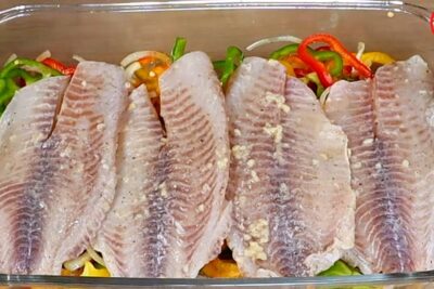Filetes de pescado crudo sobre cama de pimientos y cebolla en fuente de vidrio RfBM3gkgBP4