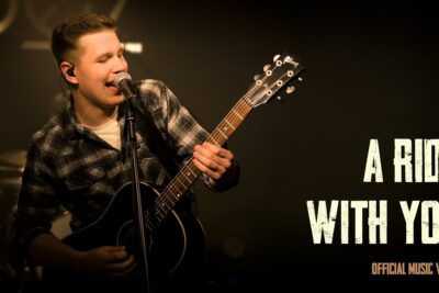 Cantante masculino tocando guitarra acústica y cantando frente a un micrófono en un escenario oscuro U14MeM0PmDA