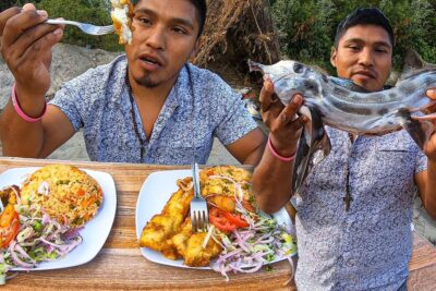 Dos hombres compartiendo pescado frito, arroz y ensalada en una mesa improvisada en la playa WLQauzerONU.