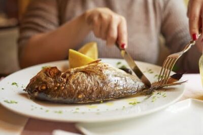 Pescado entero asado en un plato con rodajas de limón mientras una persona lo corta aHtkrNO2iuY