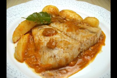 Filete de pescado en salsa roja con patatas pequeñas y hoja de laurel en un plato blanco