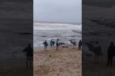 Grupo de personas en la orilla observando olas rompientes y rocas en el mar, c2zP2tnkdd4.