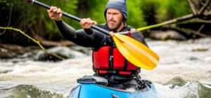 Hombre en kayak azul con chaleco rojo remando en aguas rápidas aplicando consejos evitar olas mojen pescas kayak para mantener estabilidad.