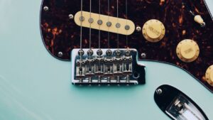 Primer plano del puente, cuerdas y perillas de una guitarra eléctrica celeste en detalle, crecimiento del bass cuanto tarda alcanzar tamano maximo