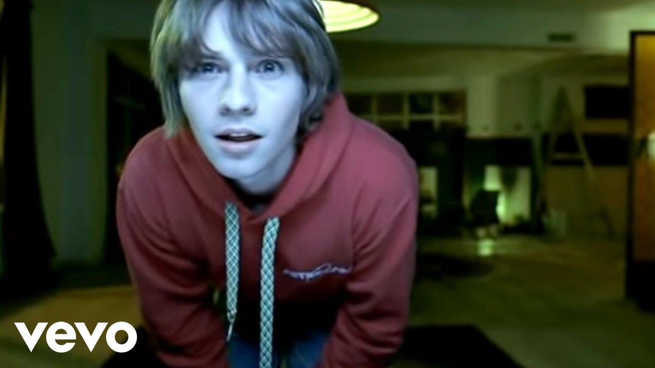 Joven con sudadera roja inclinándose hacia la cámara en interior dDj7DuHVV9E