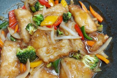 Filetes de pescado empanado en salsa brillante con brócoli, pimientos, zanahoria y cebolla