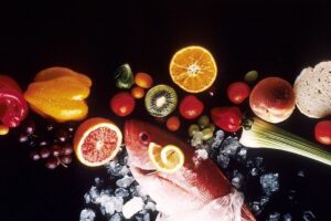 Pescado sobre hielo acompañado de rodajas de naranja, kiwi, uvas y verduras, ideal para especies peces hielo pesca lagos agua salada