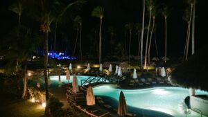 Piscina iluminada en un resort tropical por la noche entre palmeras y tumbonas, evita canas pescar enreden pesco kayak