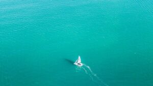 Velero solitario visto desde el aire sobre mar turquesa, guia completa mejores playas pesca kayak