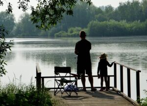 Padre y niña pescando en un muelle tranquilo frente a un lago, escena de guia completa mejores senuelos pescar carpas.