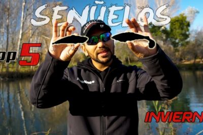 Persona junto a un lago sosteniendo dos señuelos de pesca frente a la cámara jrMrA8wW3Mg