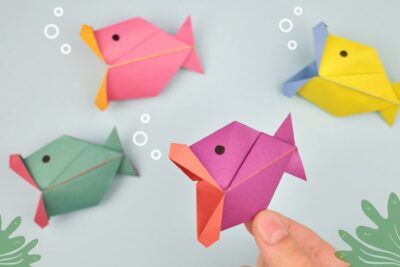 Peces origami coloridos sobre fondo azul con una mano sosteniendo un pez morado l7yd4iiRWho