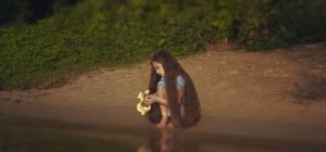 Niña sentada en la orilla del río observando el agua y su reflejo, imagen para la mejor estrategia para atrapar dorados en rios guia completa