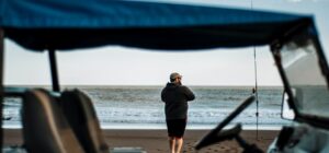 Pescador en la playa con caña junto a una embarcación, escena que invita a aprender la mejor forma de limpiar una trucha