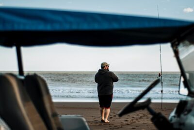 Pescador en la playa con caña junto a una embarcación, escena que invita a aprender la mejor forma de limpiar una trucha