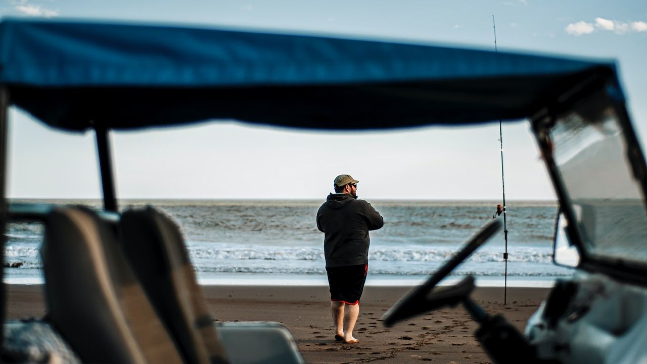 Pescador en la playa con caña junto a una embarcación, escena que invita a aprender la mejor forma de limpiar una trucha