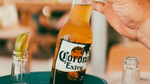 Botella de cerveza Corona Extra con gotas de condensación y rodaja de lima en mesa, mano sujetando la botella, linea pesca mosca agua salada snook guia completa