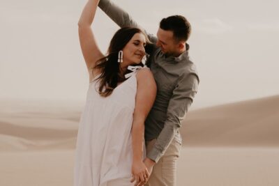 Pareja bailando en dunas al atardecer con tonos cálidos y mirada cómplice, lineas respaldo pesca agua salada mosca