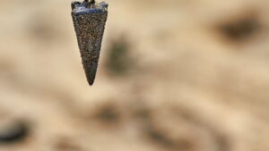 Plomo de pesca cónico cubierto de arena colgando sobre fondo arenoso difuminado los anzuelos efectivos pesca hielo descubre