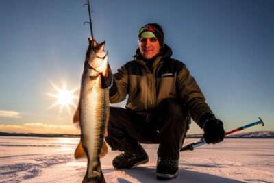 Pescador en lago congelado mostrando una lucioperca recién capturada, los mejores lugares pescar luciopercas hielo