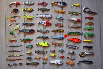 Muestra organizada de señuelos variados sobre fondo de madera en distintos colores y tamaños, los senuelos populares pesca truchas guia completa.
