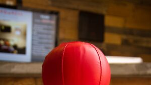 Pelota de cuero roja en primer plano sobre fondo interior desenfocado con pantalla y pared de madera, lugares populares pescar bagres