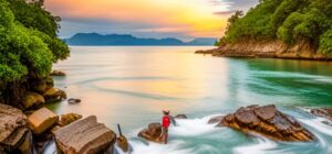 Pescador solitario con camiseta roja lanzando mosca desde rocas en aguas turquesa al atardecer, mejores destinos pesca mosca costa rica encuentra lugares