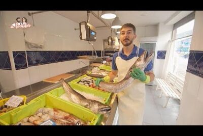 Vendedor en mercado sujetando un pescado grande ngGzRQu LwQ junto a bandejas de mariscos frescos.