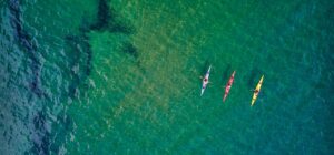 Tres kayaks coloridos y palistas en aguas turquesas vistos desde arriba, ideal para pesca en kayak principiantes