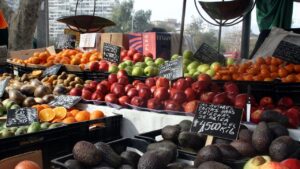 Puesto de mercado al aire libre con cajas de aguacates, manzanas, naranjas y carteles de precios a mano, peso maximo recomendado para pescar en kayak consejos y tips