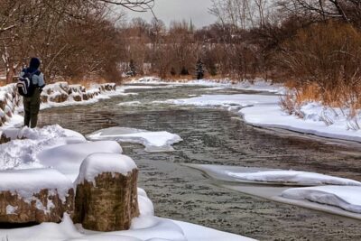Persona junto a un río parcialmente congelado en paisaje nevado que ilustra reglas comunes pesca hielo