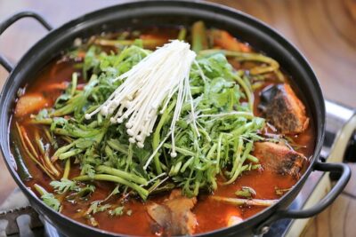 Olla con caldo rojo, trozos de pescado, hongos enoki y hojas verdes, senuelos artificiales atractivos peces