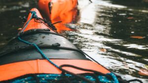 Proa de kayak naranja en el agua con cuerdas y bungee, sistemas remos kayak pesca