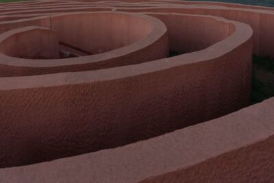 Espiral de muros texturizados color terracota formando un laberinto visto en perspectiva baja, tamano promedio lucio debes saber.