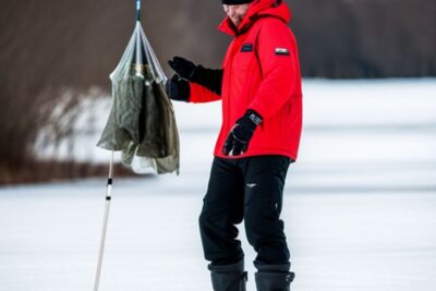 Pescador con chaqueta roja sobre un lago helado sosteniendo una red de captura, tecnicas pesca hielo mejores estrategias