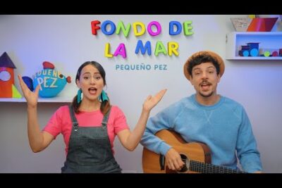 Dos presentadores infantiles cantando junto a letras coloridas 'Fondo de la mar' y un guitarrista con decorado de peces uCqQqdgsbN8