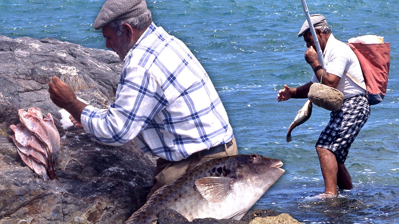 Dos pescadores limpiando y colgando filetes de pescado en unas rocas junto al mar xiO9r6DJqqs
