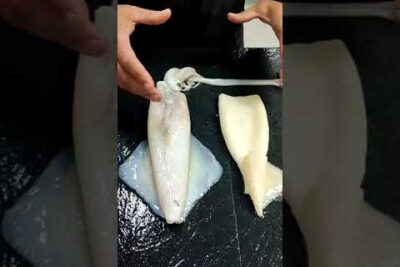 Manos limpiando calamares con la pluma translúcida retirada yD6 EzNMxkQ sobre una tabla negra.