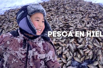 Niño abrigado y sonriente junto a una enorme pila de peces sobre el hielo zMn1lvTgEMY.