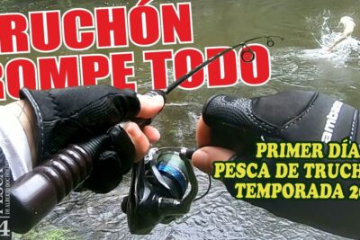 Manos enguantadas sosteniendo una caña y carrete con un gran salto en el agua durante la pesca zbyPwoAZLMY